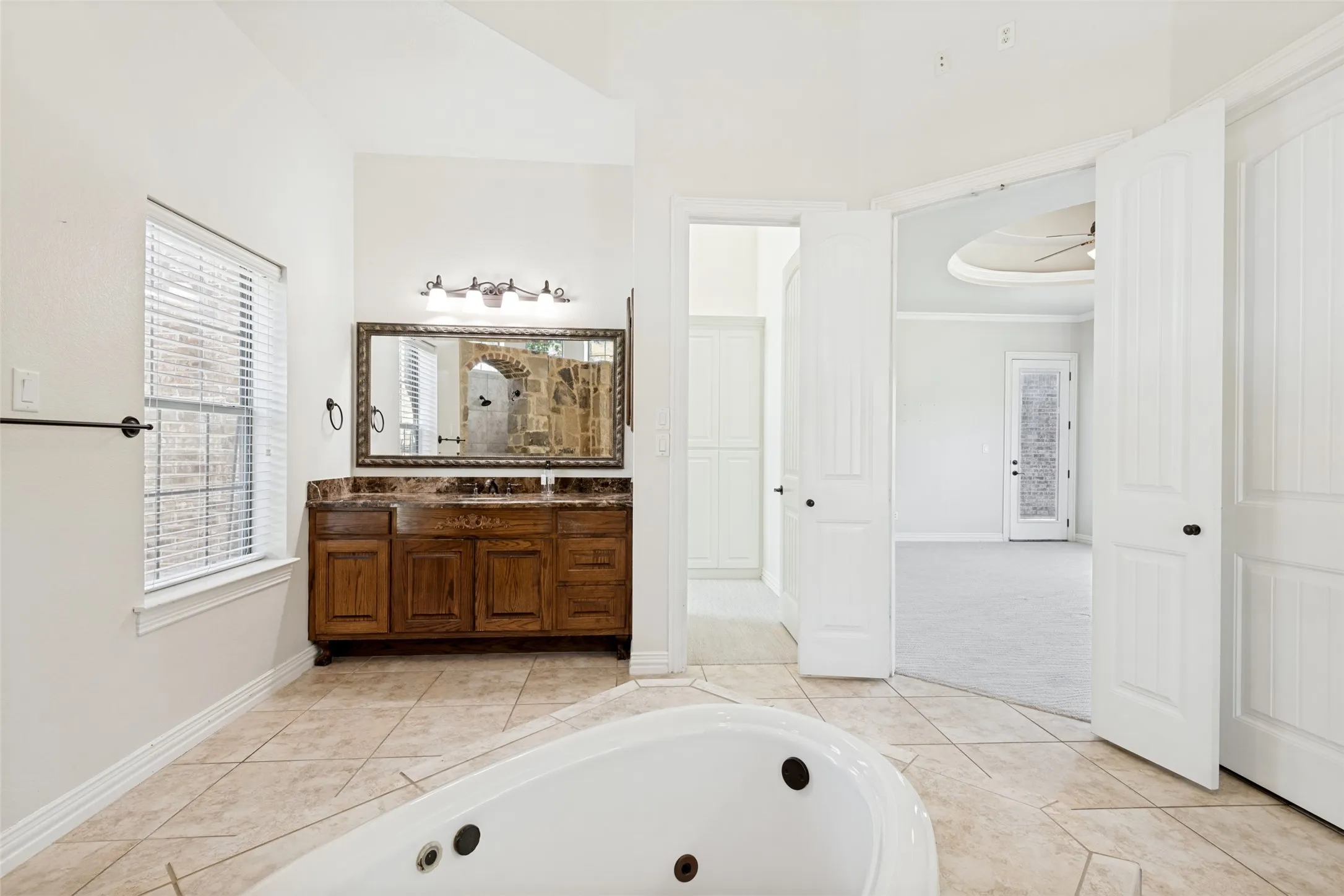 Soaking tub, dual-sink vanity with stone countertop, wood cabinetry, tile flooring, and vaulted ceiling