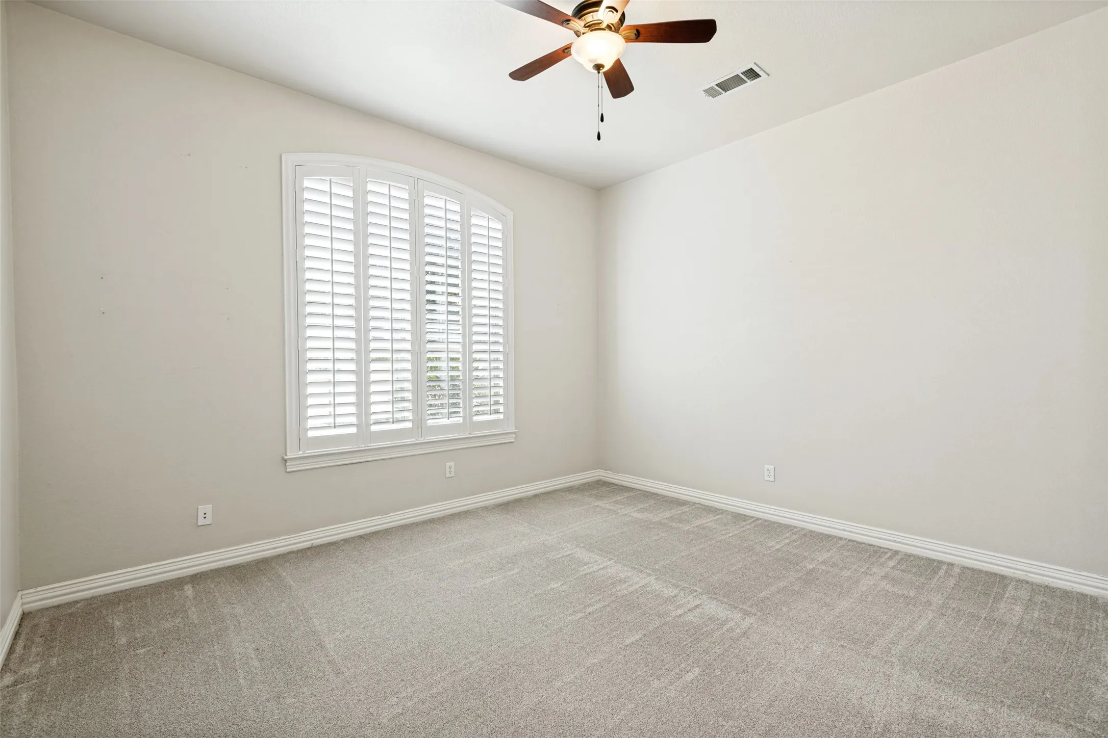 Arch-top window with plantation shutters, ceiling fan with light fixture, neutral wall color, and carpeted flooring