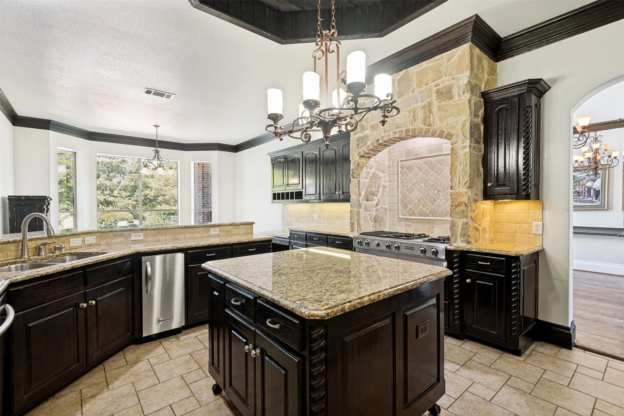 Kitchen featuring dark wood cabinetry, light-toned countertops, a central island, stainless steel appliances, and stone archway detailing