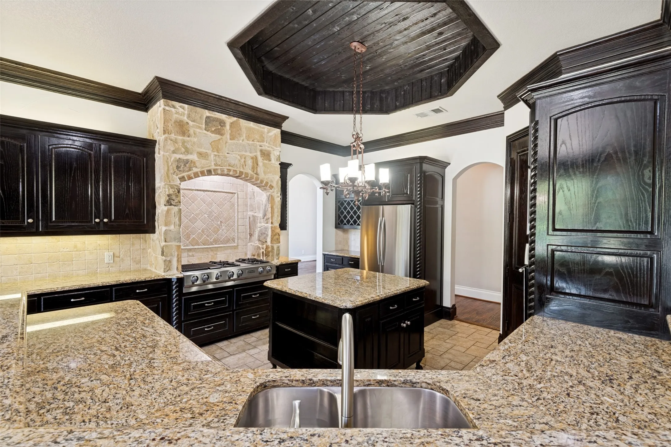 Kitchen featuring dark wood cabinetry, granite countertops, a stone-clad range hood, stainless steel appliances, and a wood-paneled coffered ceiling