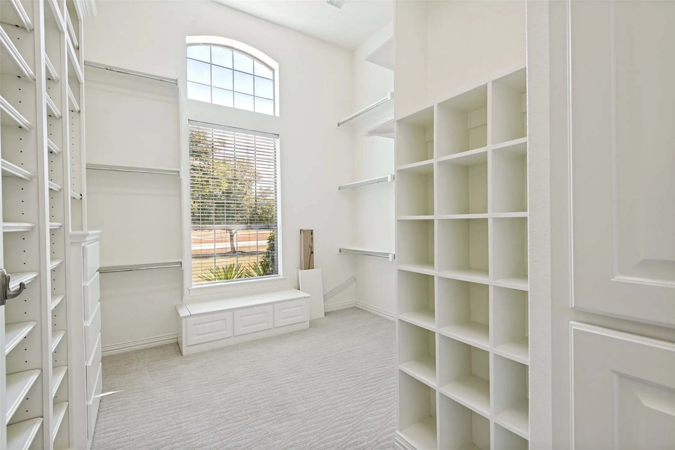 Vaulted ceiling with an arched window, built-in window seating, custom shelving units, and plush carpeting