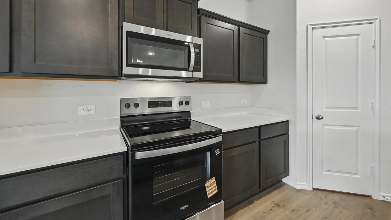 Stainless steel microwave, electric range, dark wood-finish cabinetry, light-toned countertops, and wood-finish flooring
