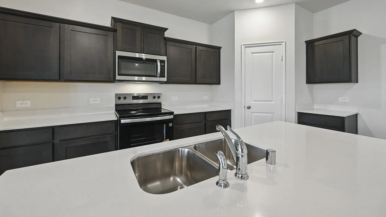 Kitchen featuring dark wood-finish cabinetry, light-toned countertops, stainless steel appliances, and a dual-basin sink with a chrome faucet