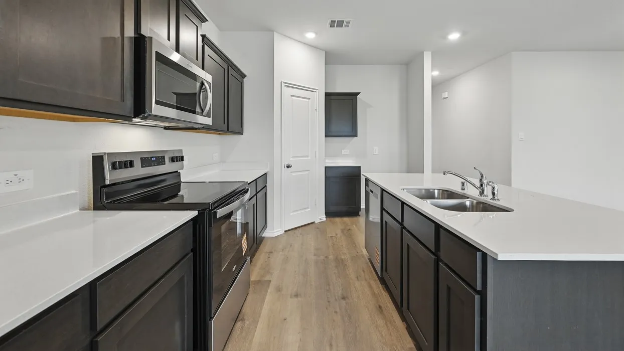 Kitchen featuring wood-finish flooring, dark cabinetry, light countertops, stainless steel appliances, and a double basin sink