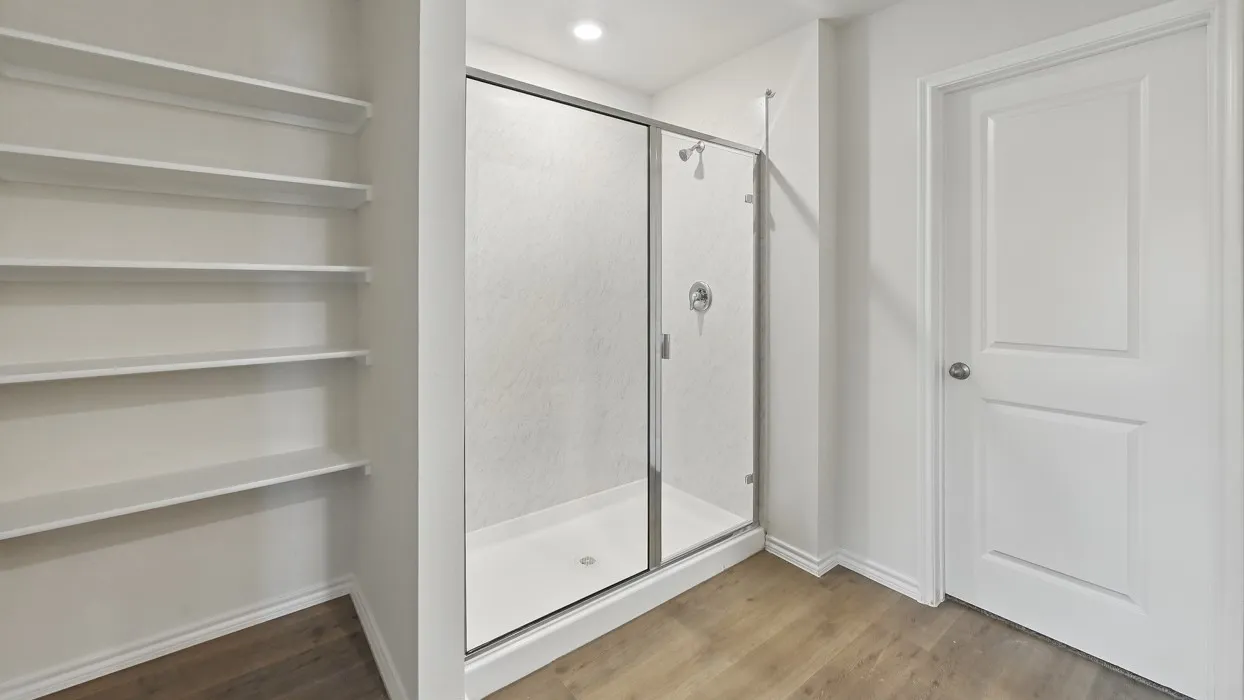 Built-in open shelving, glass-enclosed shower, white paneled door, wood-finish flooring, and recessed ceiling lighting