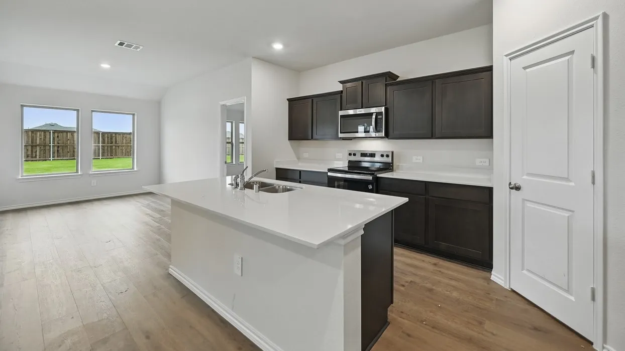 Kitchen featuring an island with a double basin sink, dark wood-finish cabinetry, stainless steel appliances, and a light-toned countertop