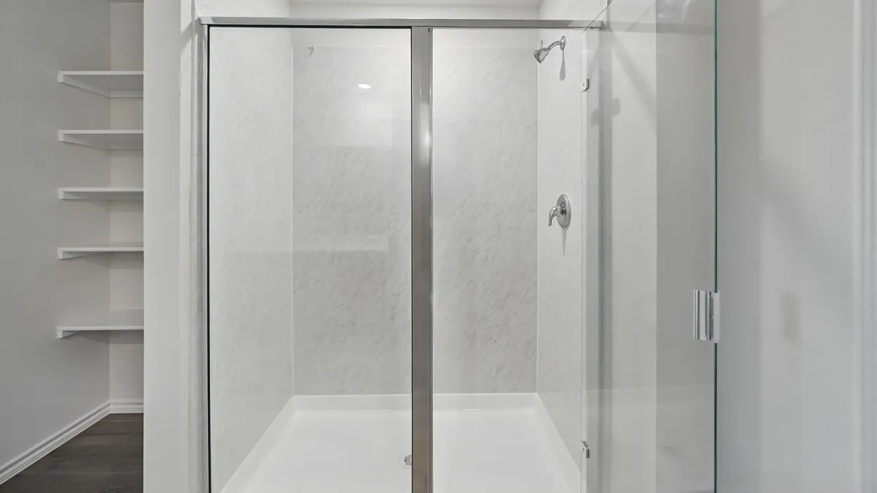 Glass-enclosed shower with a chrome shower head and handle, white shower pan, and built-in shelving