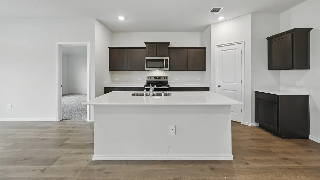 Kitchen with wood-finish flooring, dark wood cabinetry, white countertops, and a large central island featuring a stainless steel sink