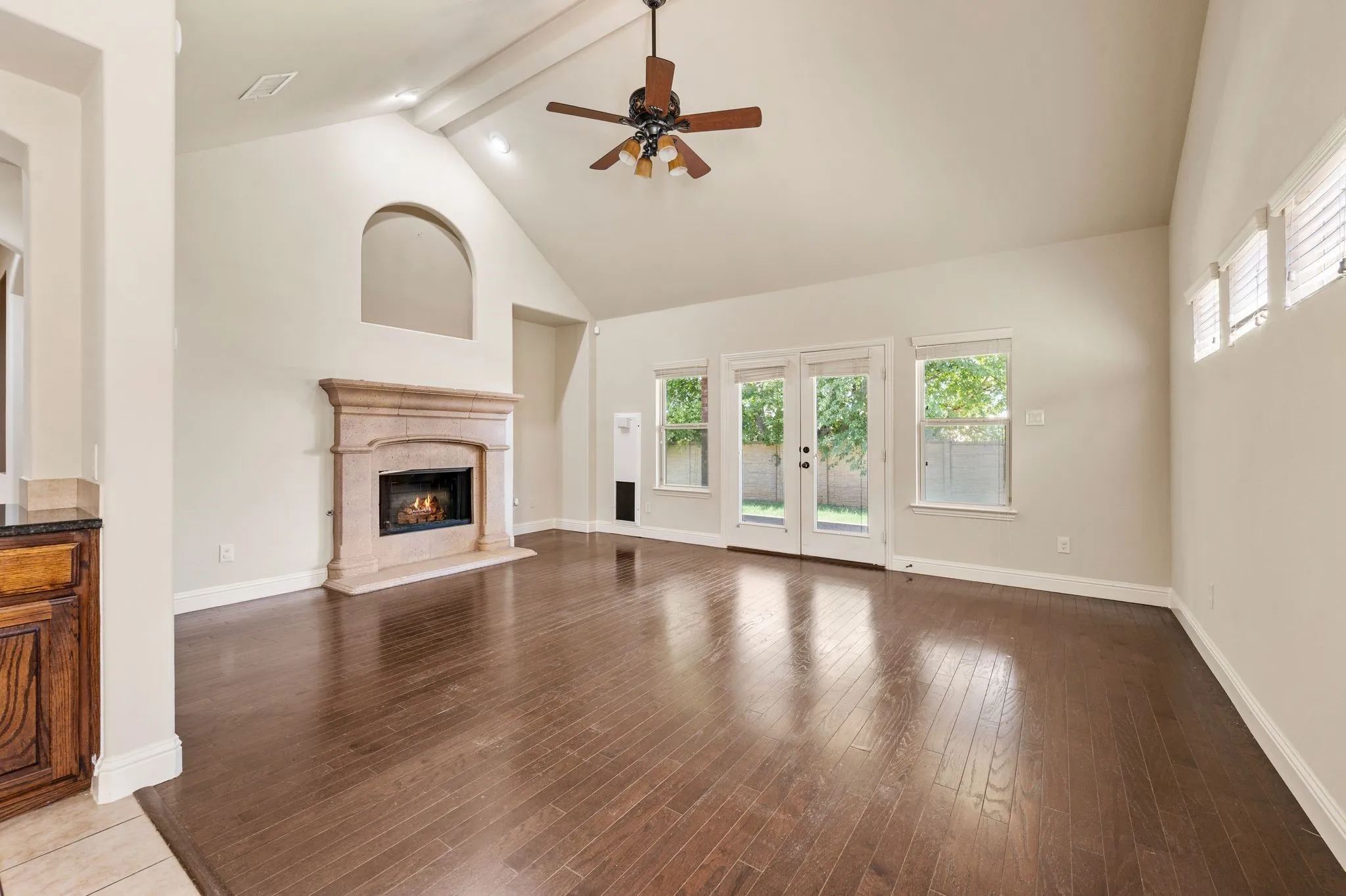 Vaulted ceiling with exposed beam, wood-finish flooring, stone fireplace with hearth, built-in cabinetry with granite countertop, and French doors