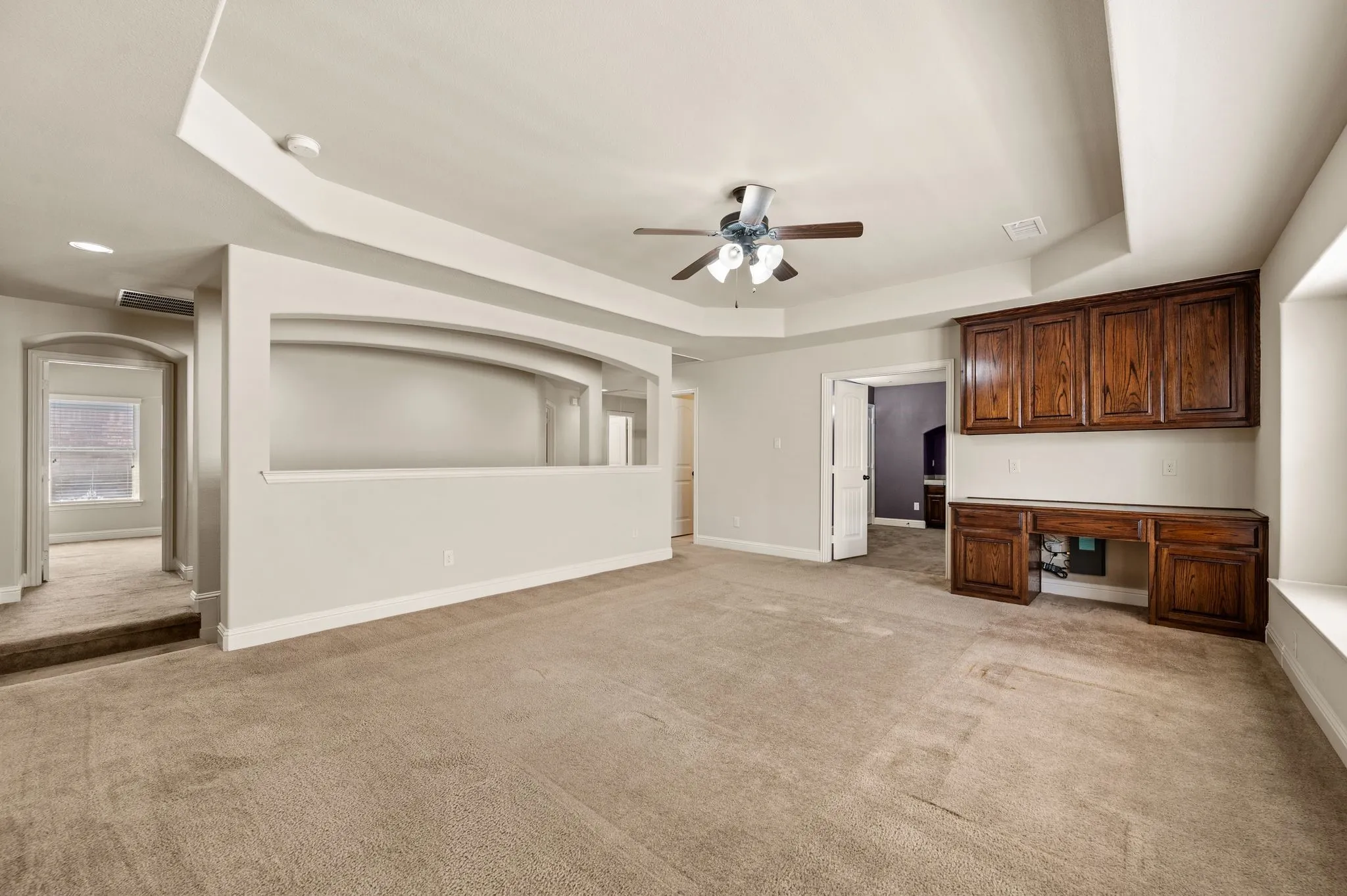 Tray ceiling, ceiling fan with light fixture, built-in cabinetry, built-in desk, and neutral carpeting