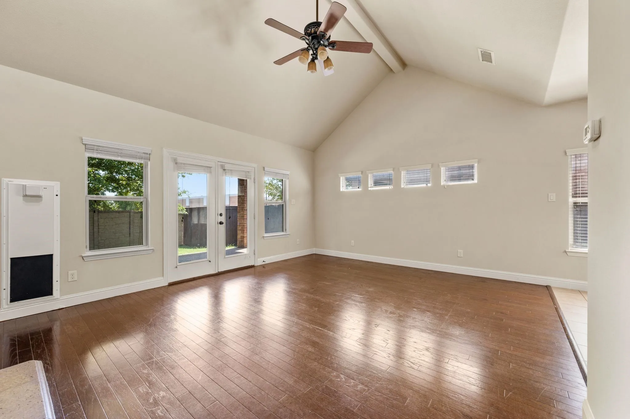 Vaulted ceiling with exposed beam, wood-finish flooring, ceiling fan, and multiple windows