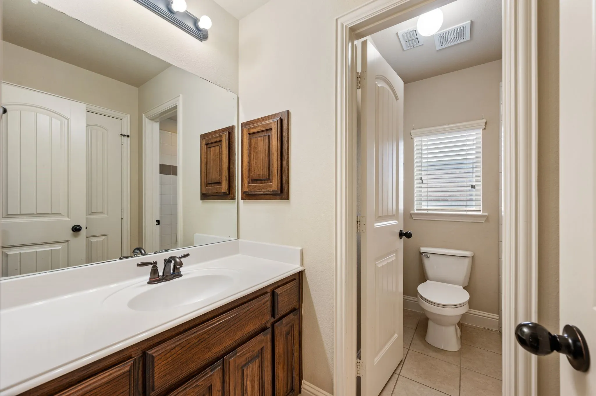 Bathroom vanity featuring a wood-finish cabinet, white countertop with integrated sink, and bronze-finish faucet