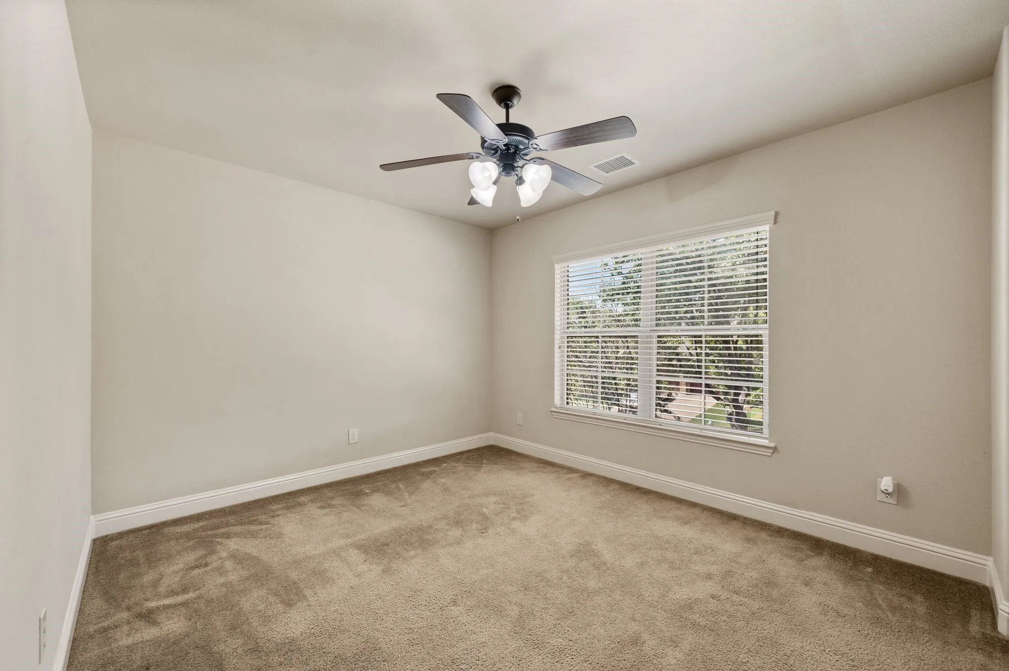 Neutral wall color with plush carpeting, featuring a ceiling fan with integrated lighting