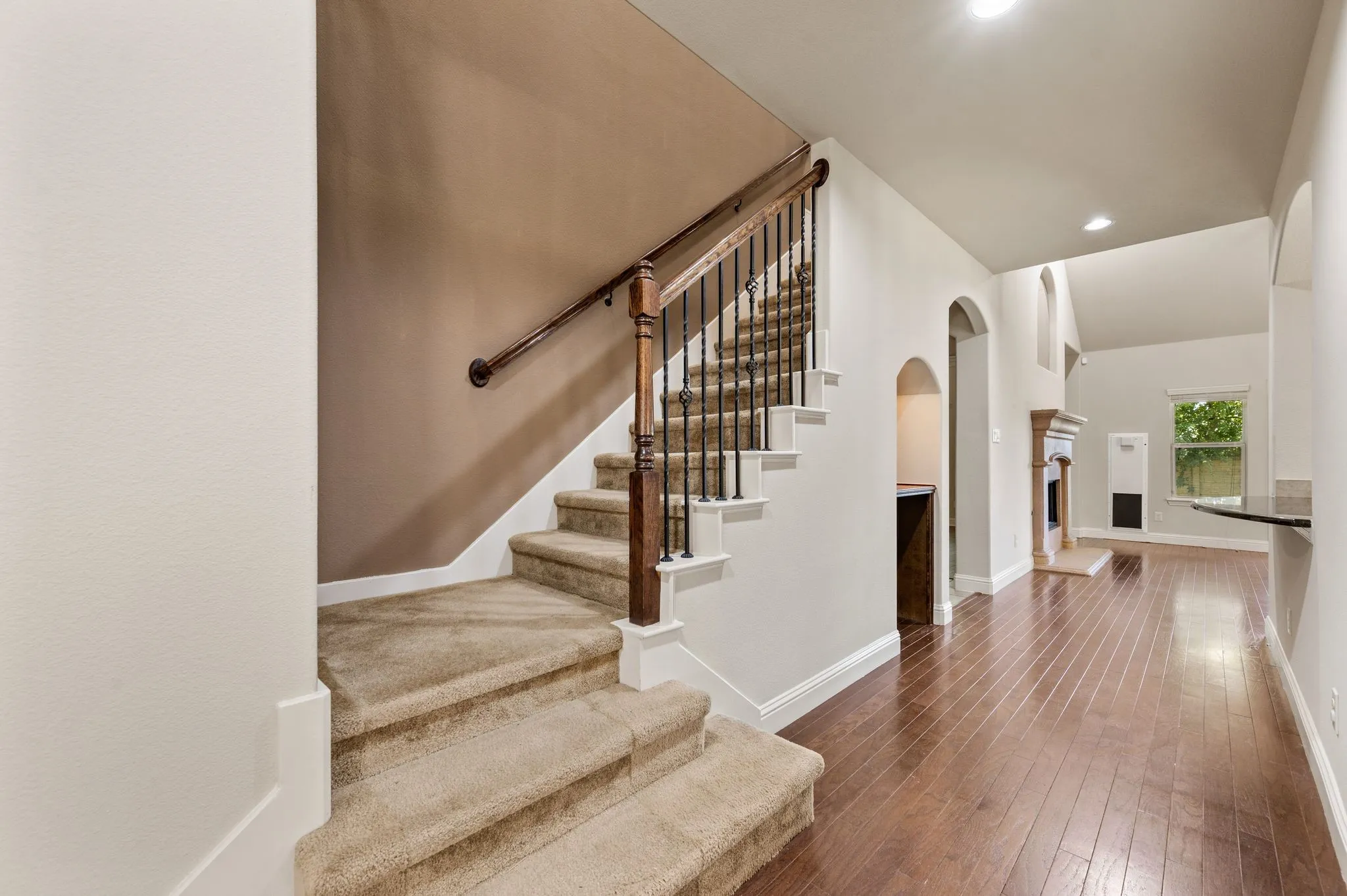 Hardwood flooring, carpeted staircase with wood handrail, wrought iron balusters, arched entryways, and a built-in fireplace
