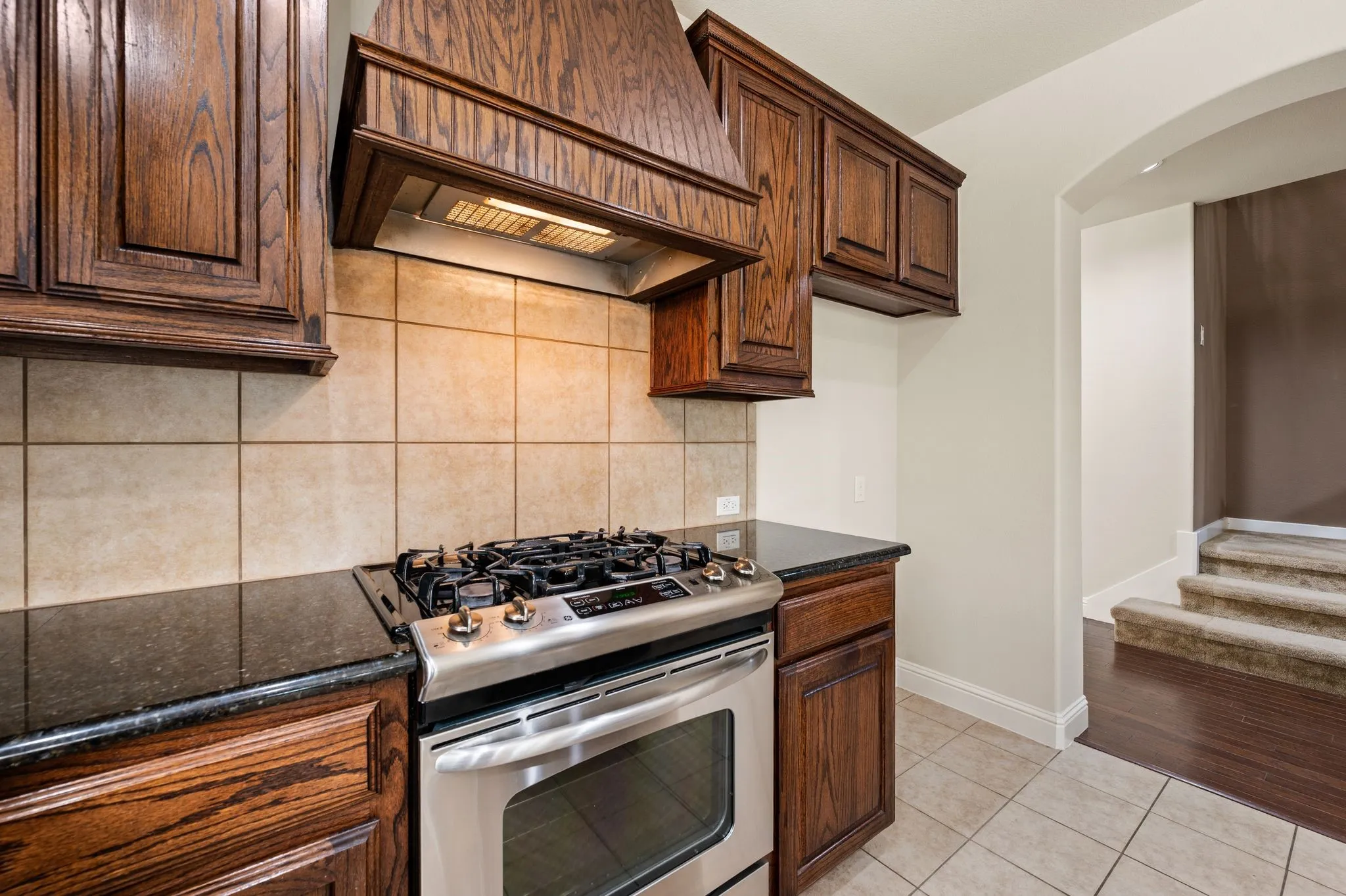 Stainless steel range with a gas cooktop, dark wood cabinetry, dark countertops, tiled backsplash, and tiled flooring