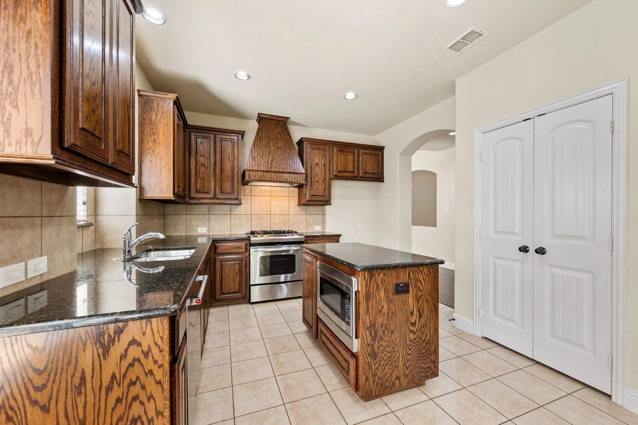 Kitchen featuring wood cabinetry, dark countertops, a central island with microwave, and stainless steel appliances