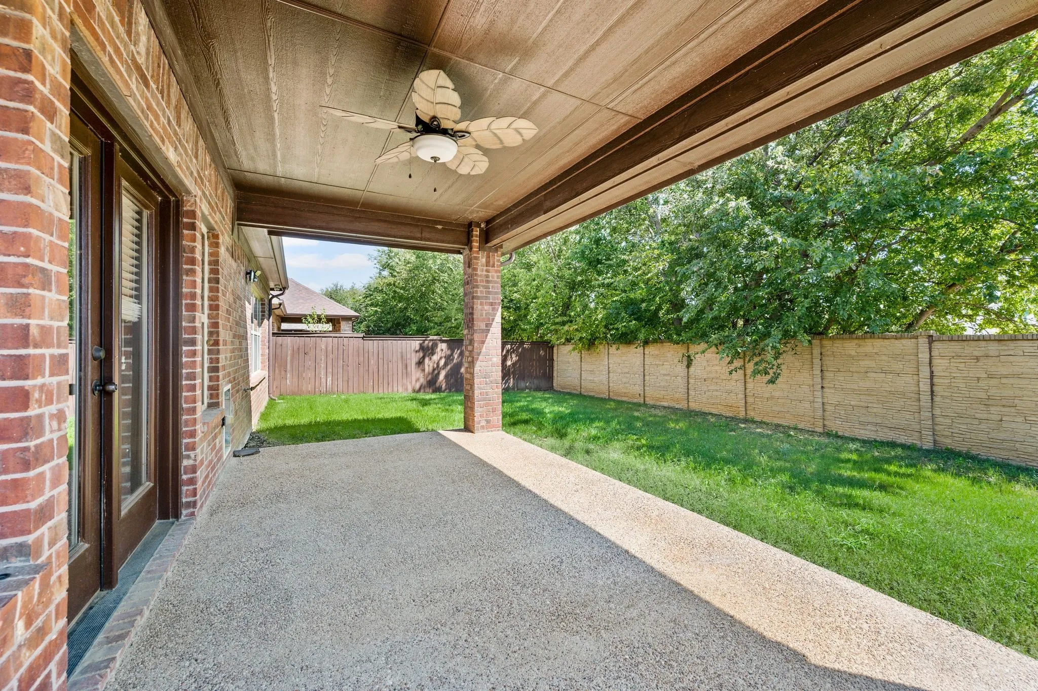 Covered patio with a ceiling fan, brick exterior, and a stone privacy fence