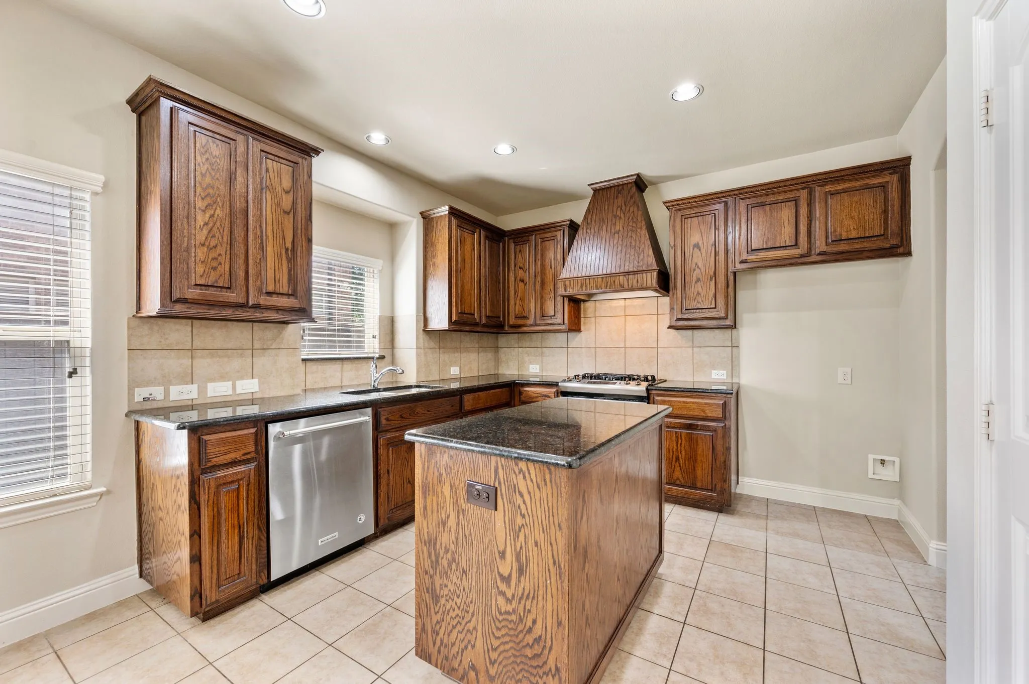 Kitchen featuring warm wood cabinetry, granite countertops, tile flooring, stainless steel dishwasher, and recessed lighting