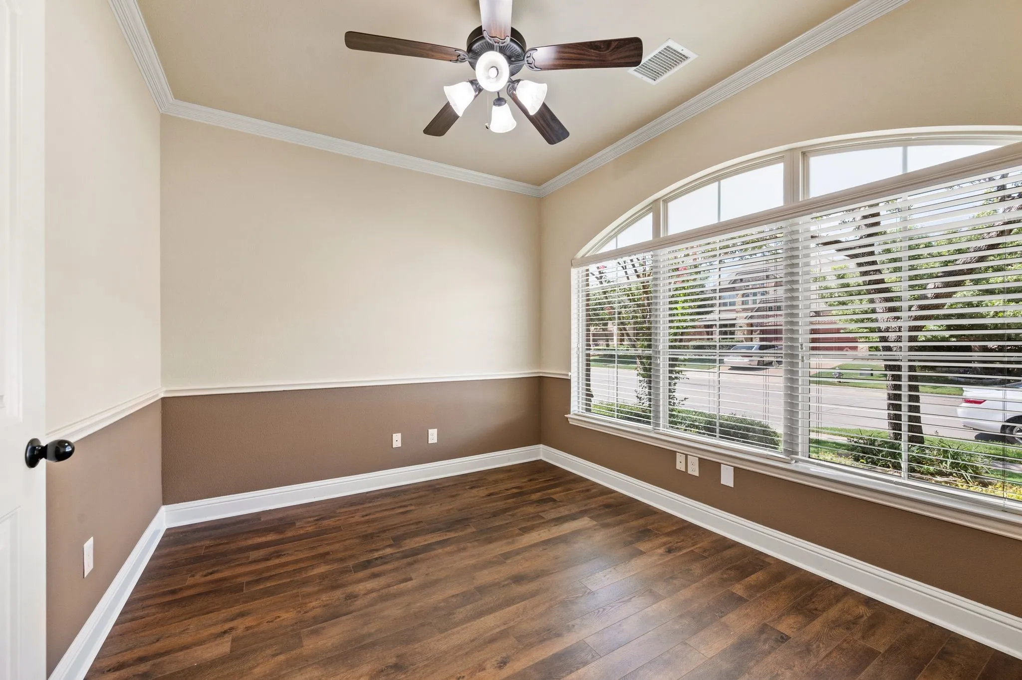 Arched window with blinds, wood-finish flooring, two-tone wall treatment, crown molding, and a ceiling fan