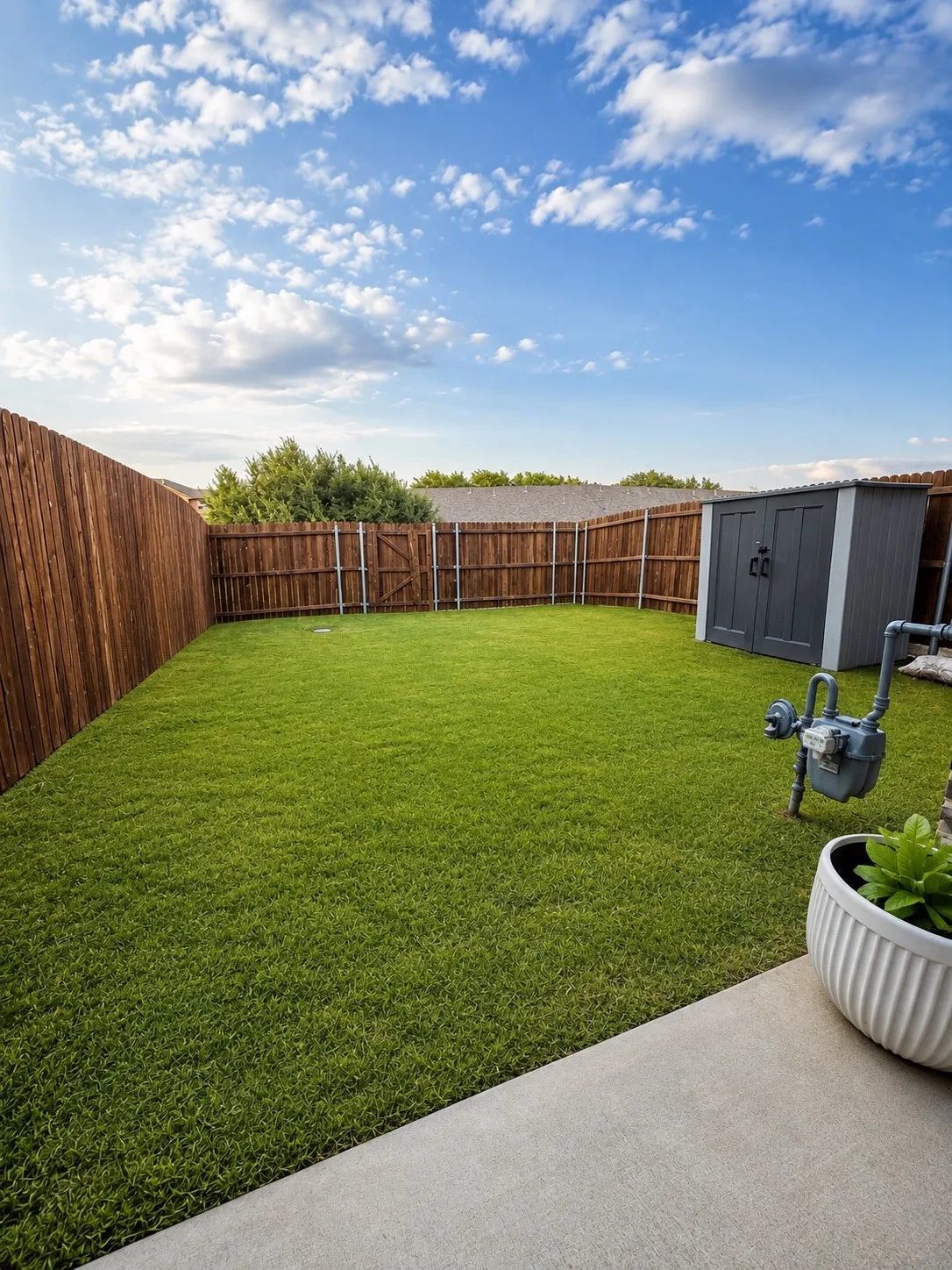 Expansive backyard featuring a manicured lawn, wood-paneled perimeter fencing, a gate, a storage shed, and a concrete patio