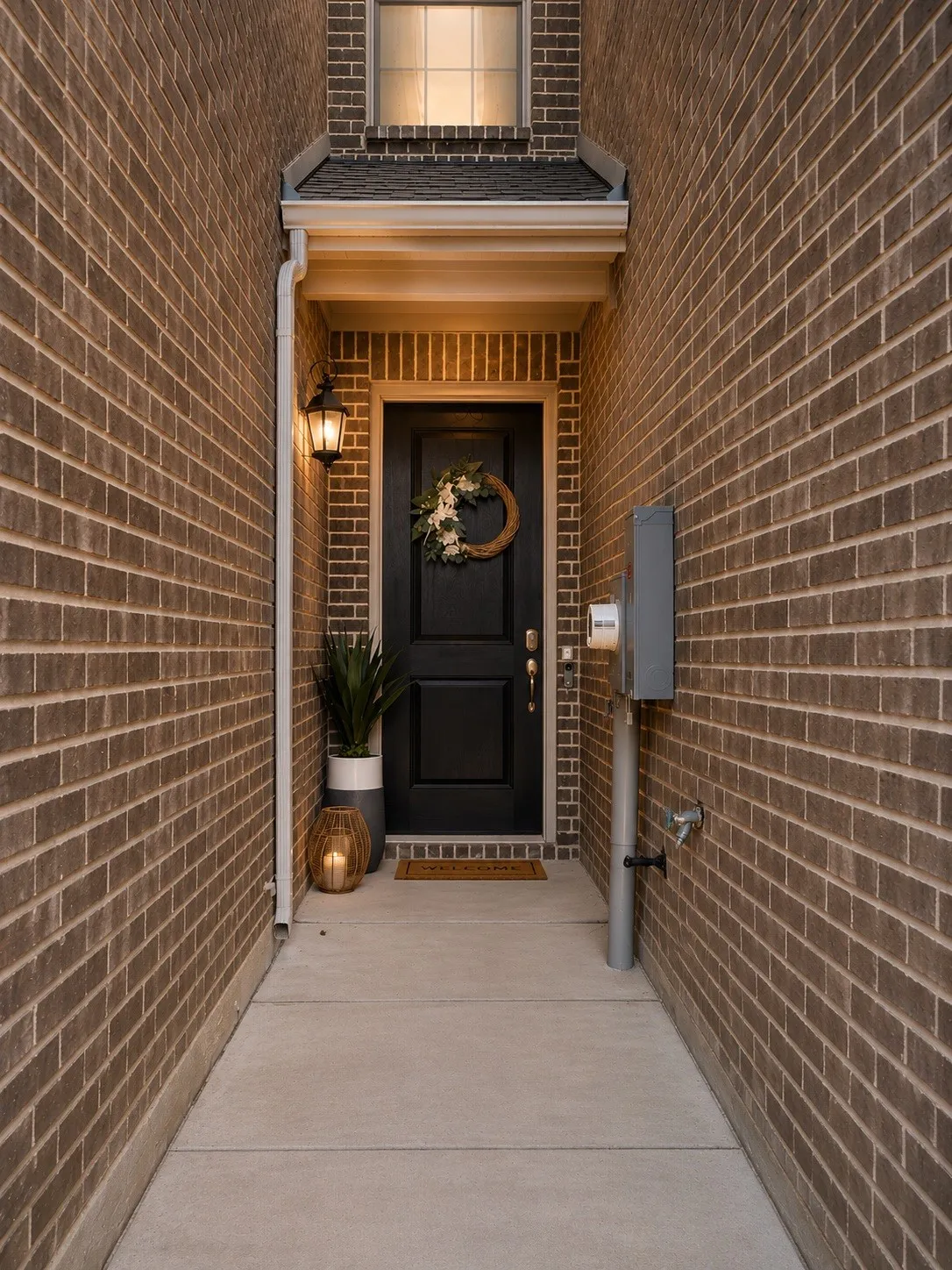 Brick exterior with a covered entry, dark paneled front door, and an exterior wall lantern