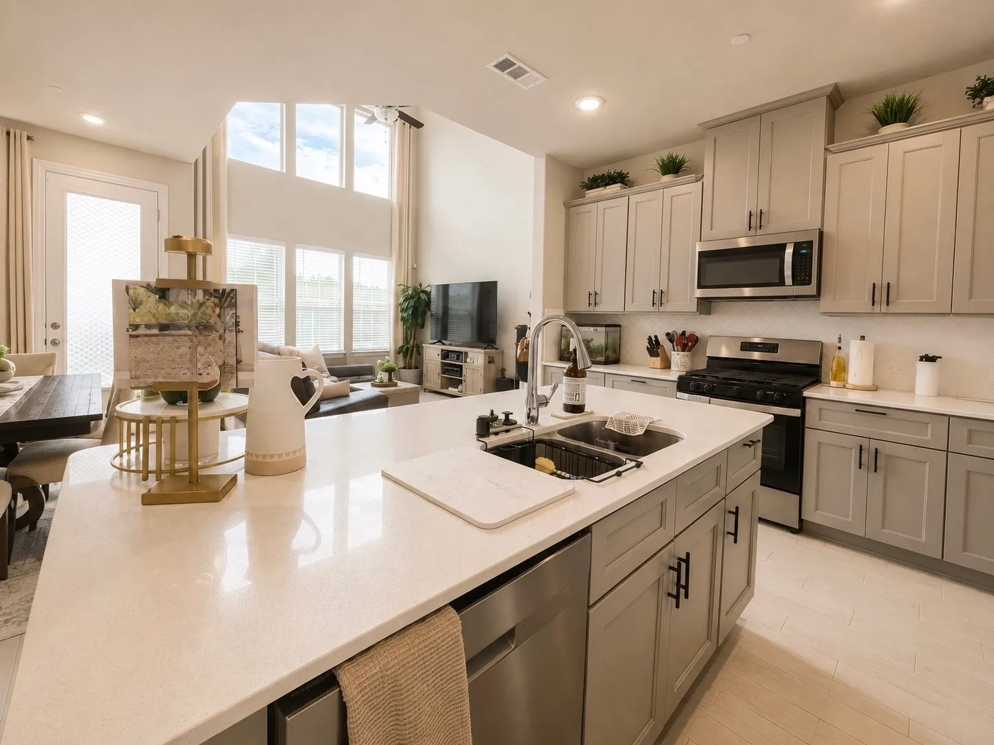 Kitchen featuring light gray cabinetry, stainless steel appliances, a center island with sink, and light-toned countertops