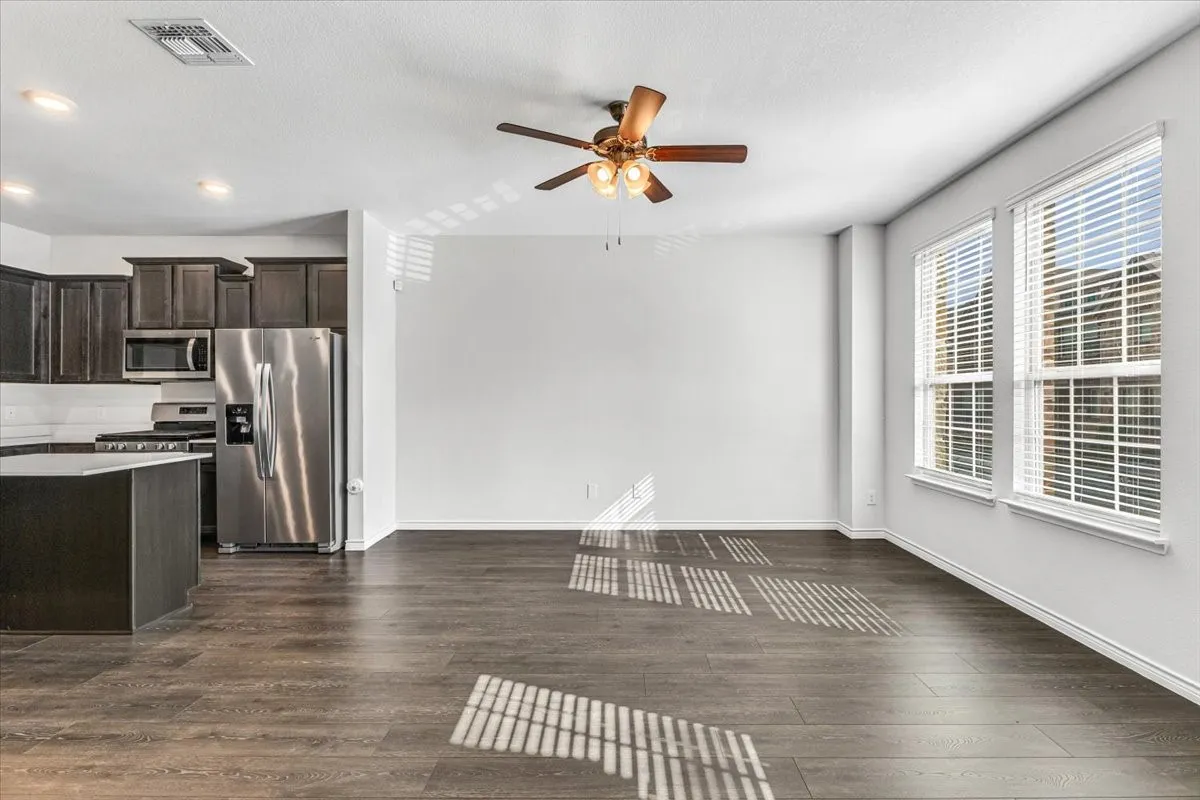 Open concept living area featuring wood-finish flooring, two large windows with blinds, and a ceiling fan