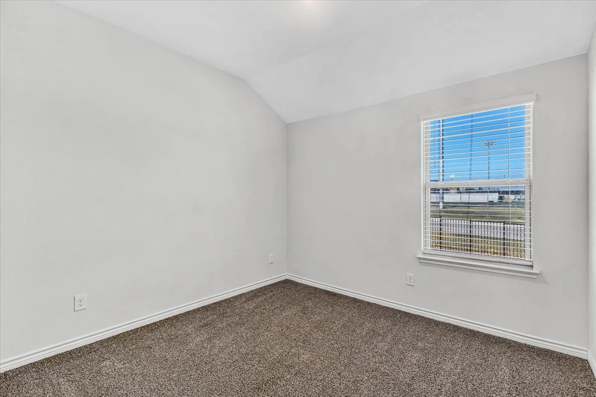 Carpeted flooring with light-colored walls, featuring a window with horizontal blinds and a sloped ceiling