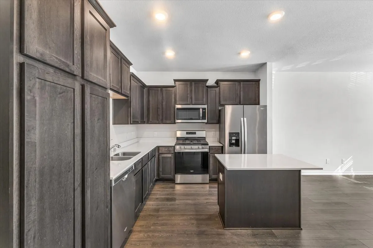 Kitchen featuring dark wood-finish cabinetry, stainless steel appliances, a white subway tile backsplash, and a central island with a white countertop