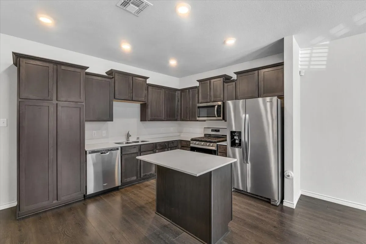 Kitchen featuring dark wood-finish cabinetry, stainless steel appliances, a center island with a light countertop, wood-finish flooring, and recessed lighting