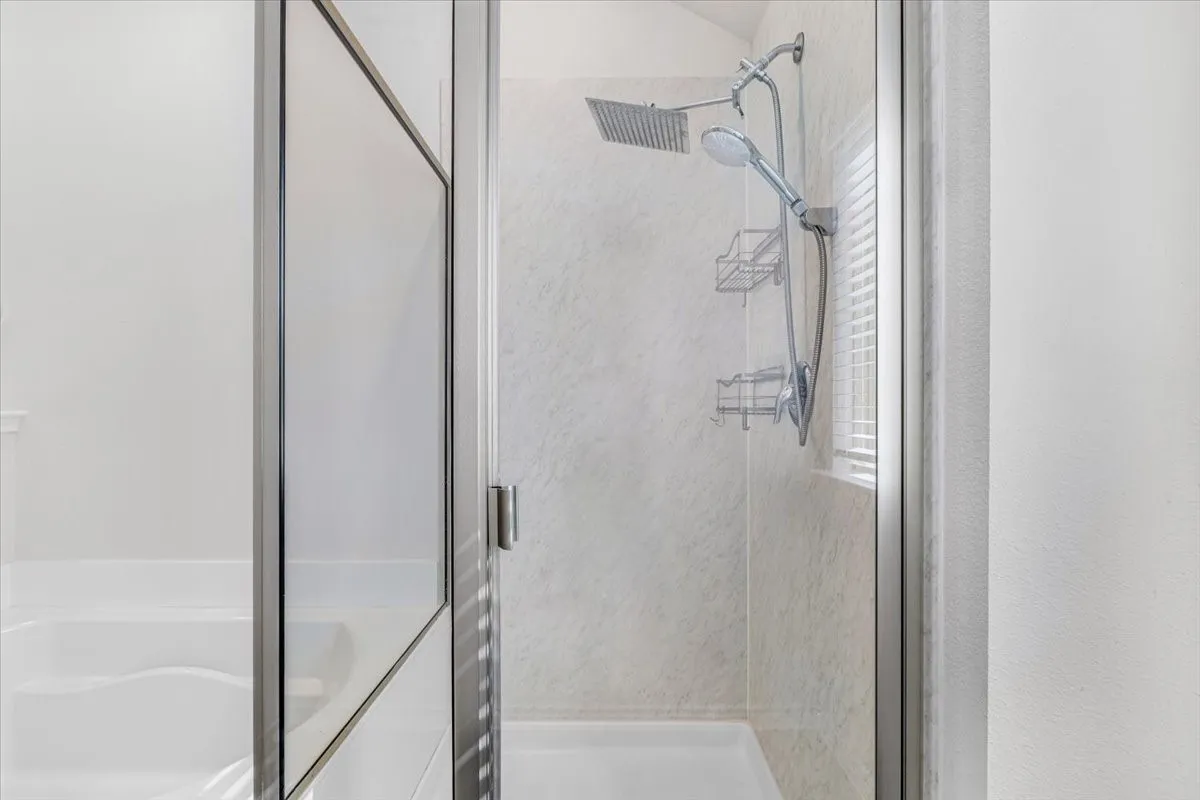 Glass-enclosed shower with a rainfall showerhead, handheld shower, and integrated shelving