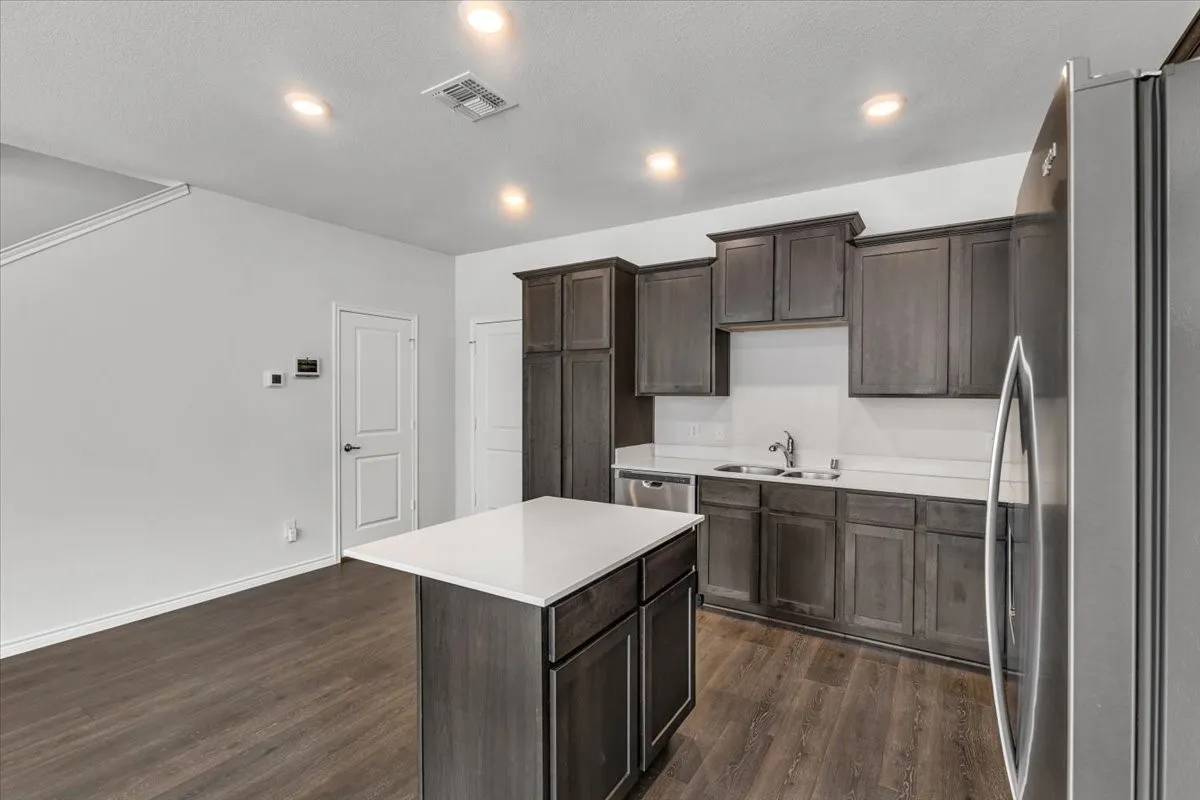Kitchen featuring dark wood-finish cabinetry, a central island with a white countertop, stainless steel appliances, and wood-finish flooring