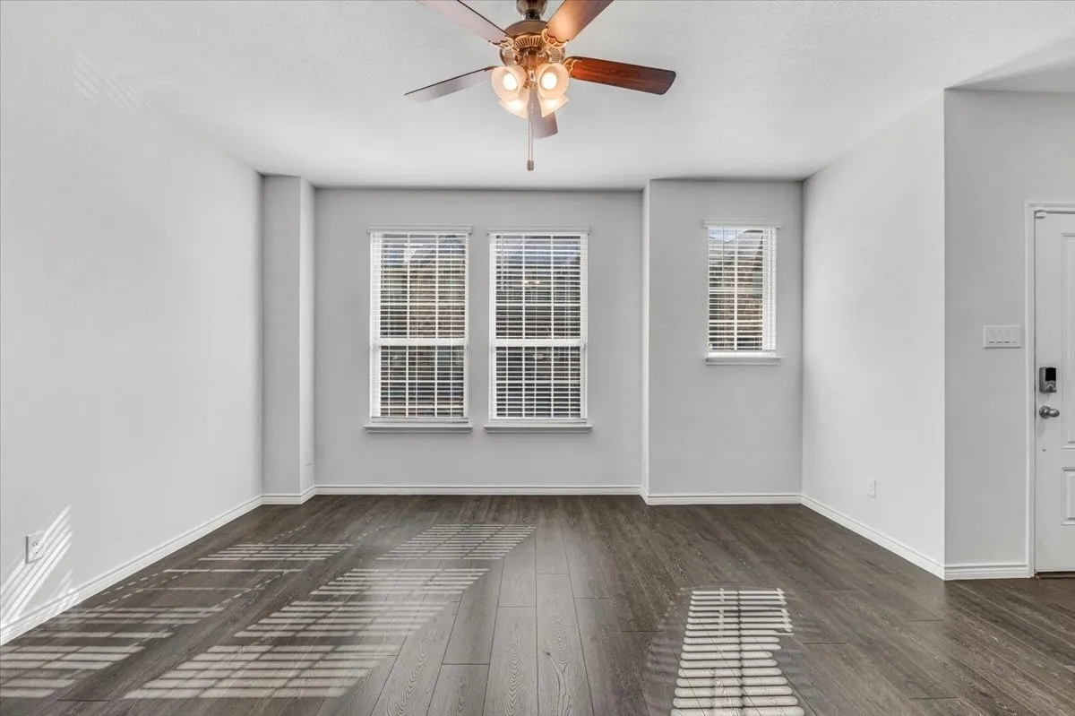 Wood-finish flooring, multiple windows with blinds, ceiling fan with light fixture, and white walls