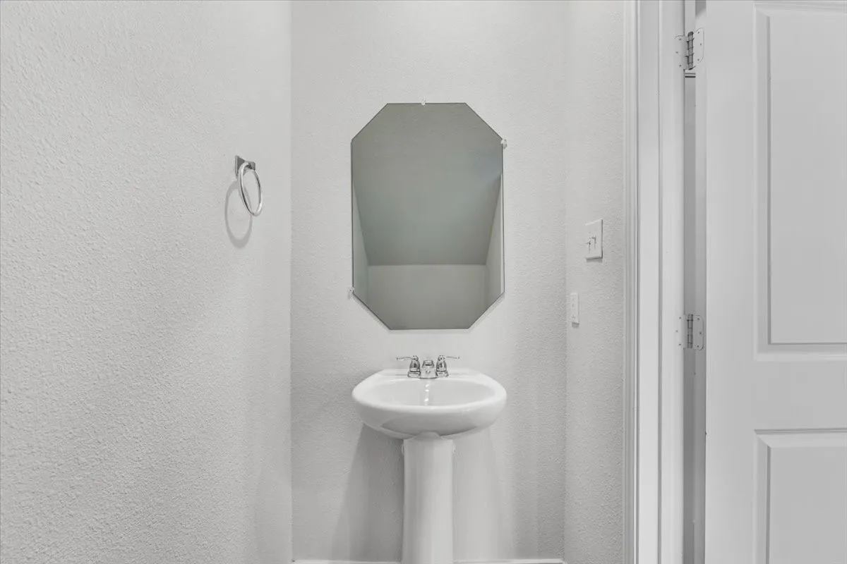 Pedestal sink with chrome faucet, octagonal mirror, and light gray textured walls