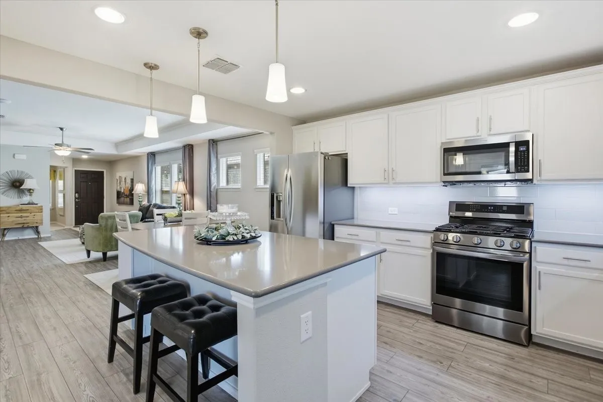 Open-concept kitchen featuring an expansive island with countertop seating, and upgraded stove/oven, white cabinetry, and quartz countertops