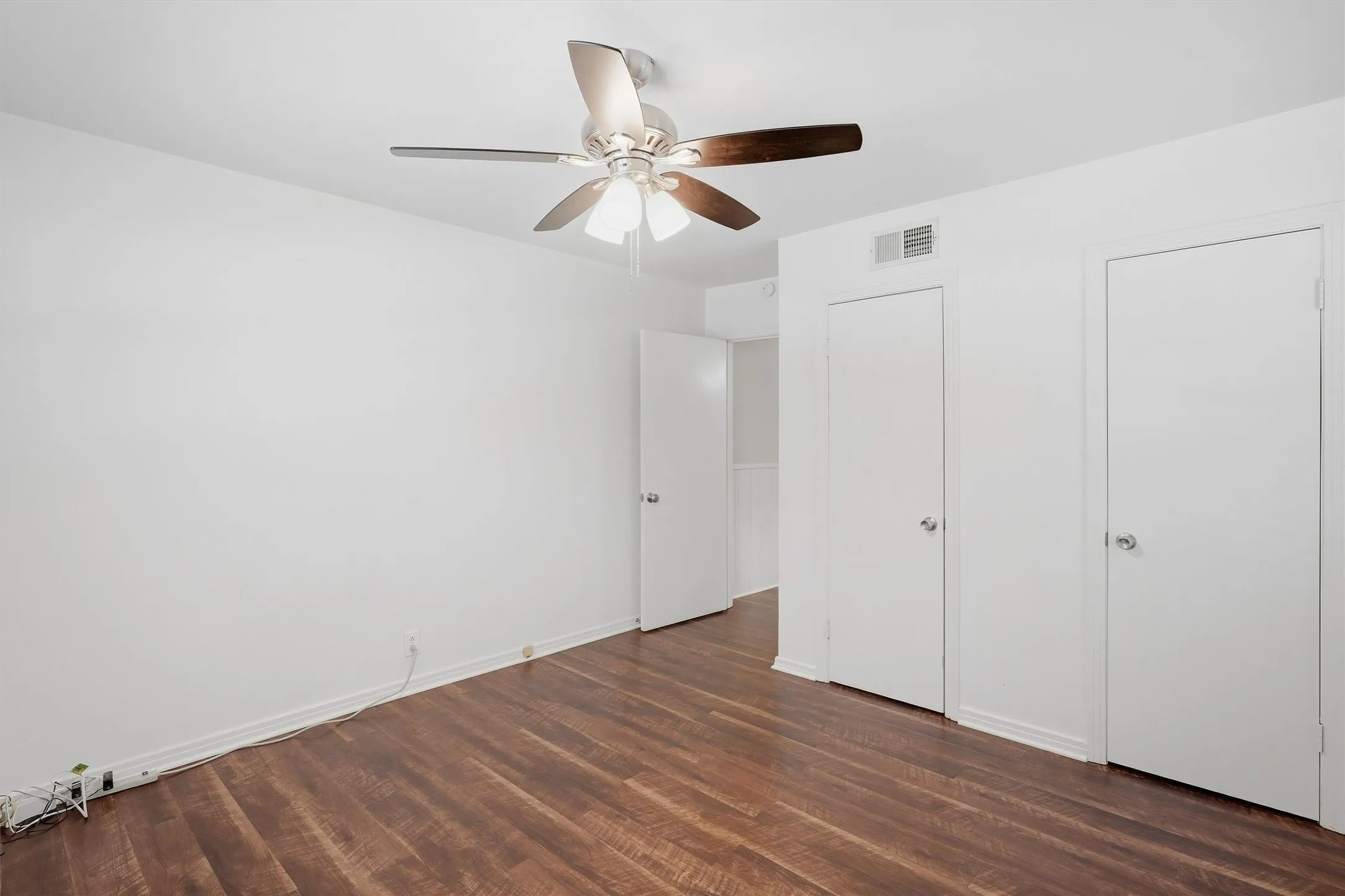 Another versatile secondary bedroom features crisp white walls, rich wood-look flooring, and a modern ceiling fan with light fixture. Multiple entry and closet doors provide excellent functional access while maintaining a bright, neutral slate ready for any decor style.