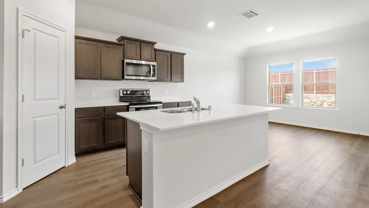 Modern kitchen featuring an island with an integrated sink, dark wood-finish cabinetry, stainless steel appliances, and white countertops