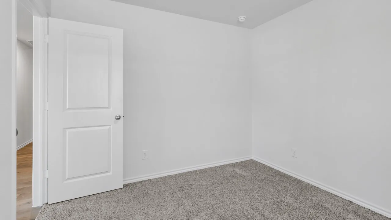 Room featuring plush gray carpeting, white painted walls, white baseboards, and a white two-panel interior door with chrome hardware