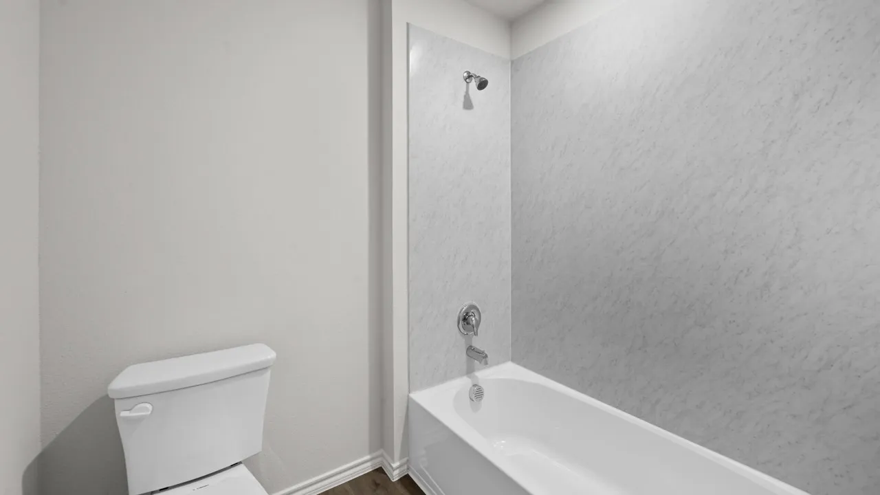 Bathroom featuring a white porcelain toilet, a white bathtub, and a shower with a chrome fixture