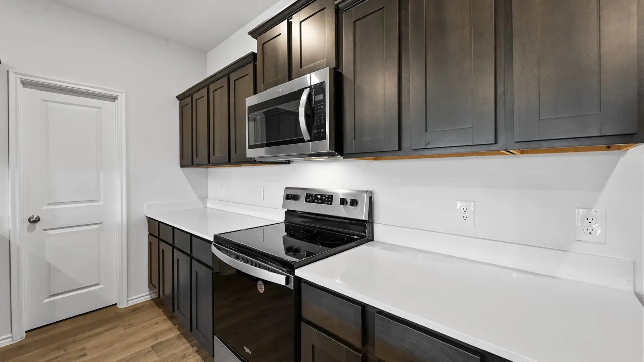 Kitchen featuring dark wood-finish cabinetry, stainless steel microwave, electric range, white countertops, and wood-finish flooring