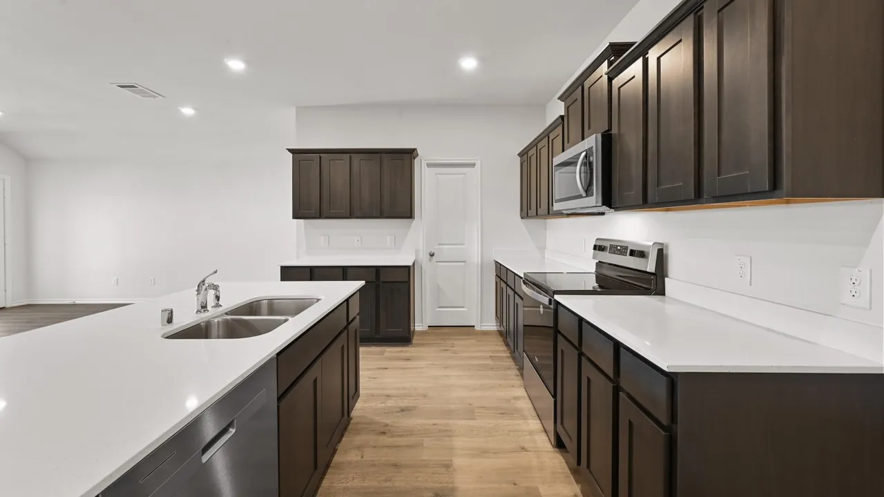 Modern kitchen featuring a large central island with a double stainless steel sink, dark wood-finish cabinetry, and light-colored countertops