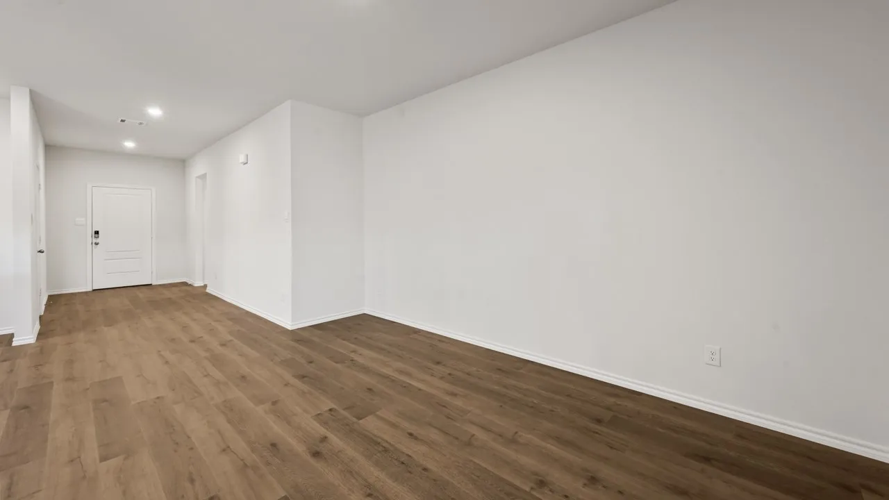 Expansive room featuring wood-finish flooring, white baseboards, recessed lighting, and a paneled entry door