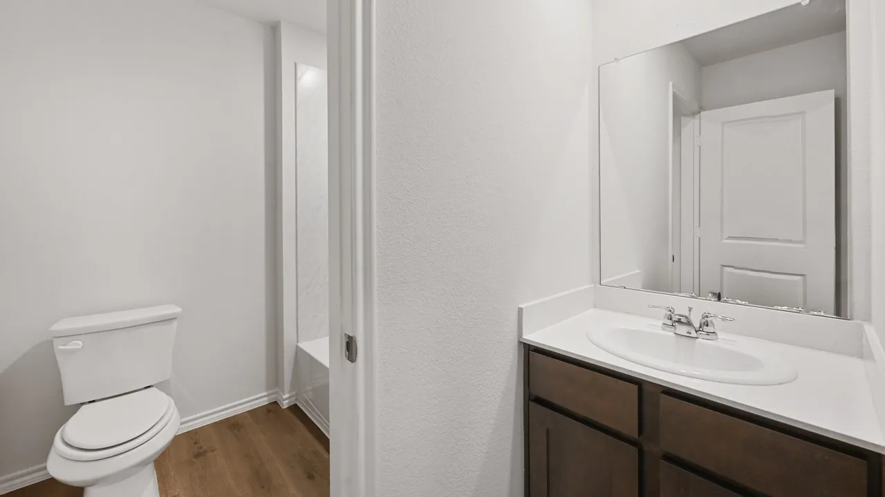 Bathroom vanity with a white countertop and integrated sink, chrome faucet, wood-finish cabinetry, and a frameless mirror