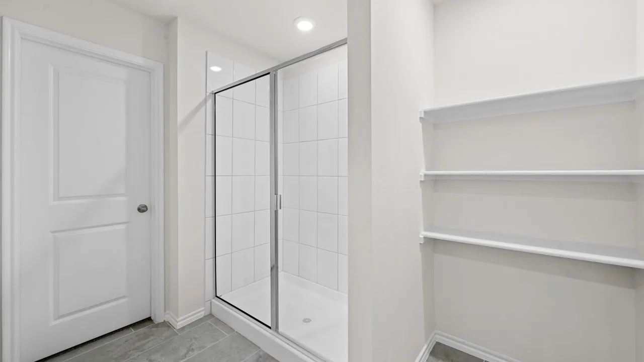 Shower enclosure with clear glass doors, white tiled walls, and recessed lighting