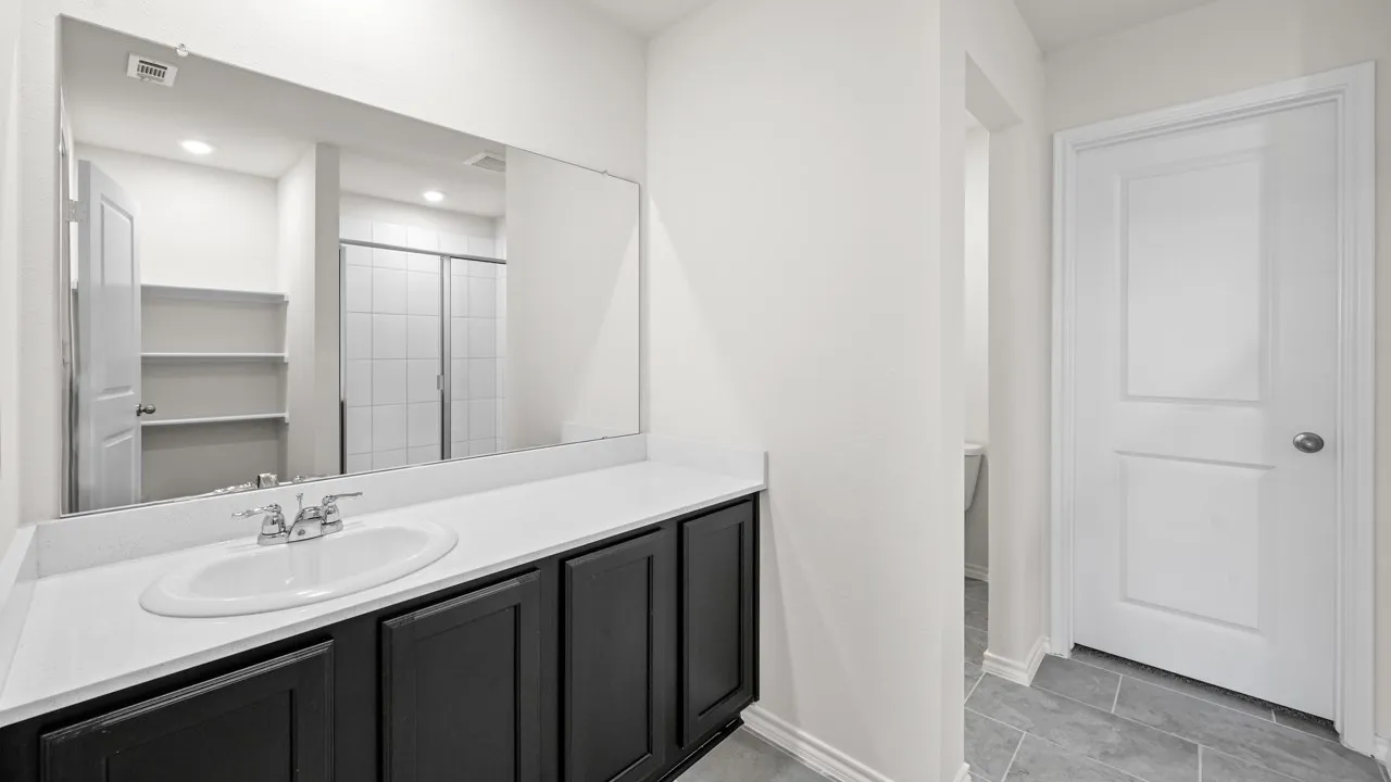 Bathroom vanity featuring a white oval sink set in a light-toned countertop, dark cabinetry, and a large wall-mounted mirror