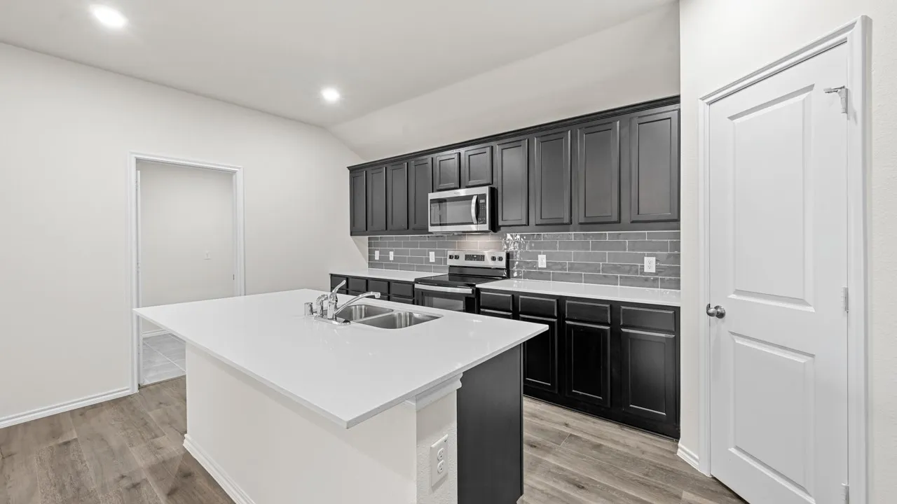 Kitchen featuring a central island with a double basin sink, dark cabinetry, light countertops, and a gray subway tile backsplash