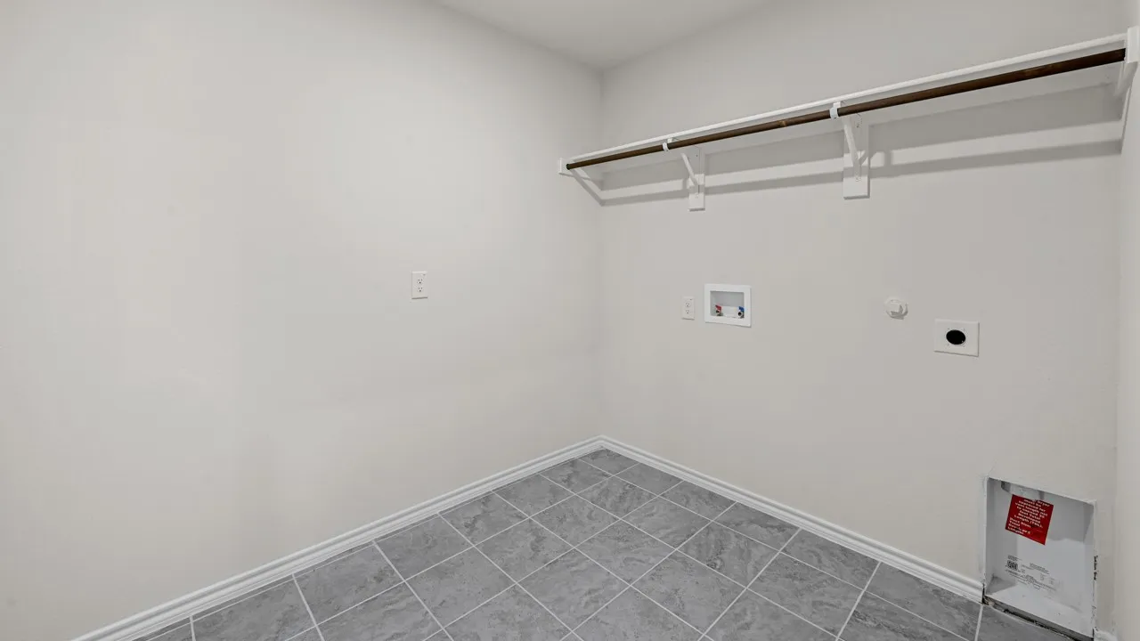 Utility room featuring grey square tile flooring, white baseboards, a single clothing rod, and a built-in shelf
