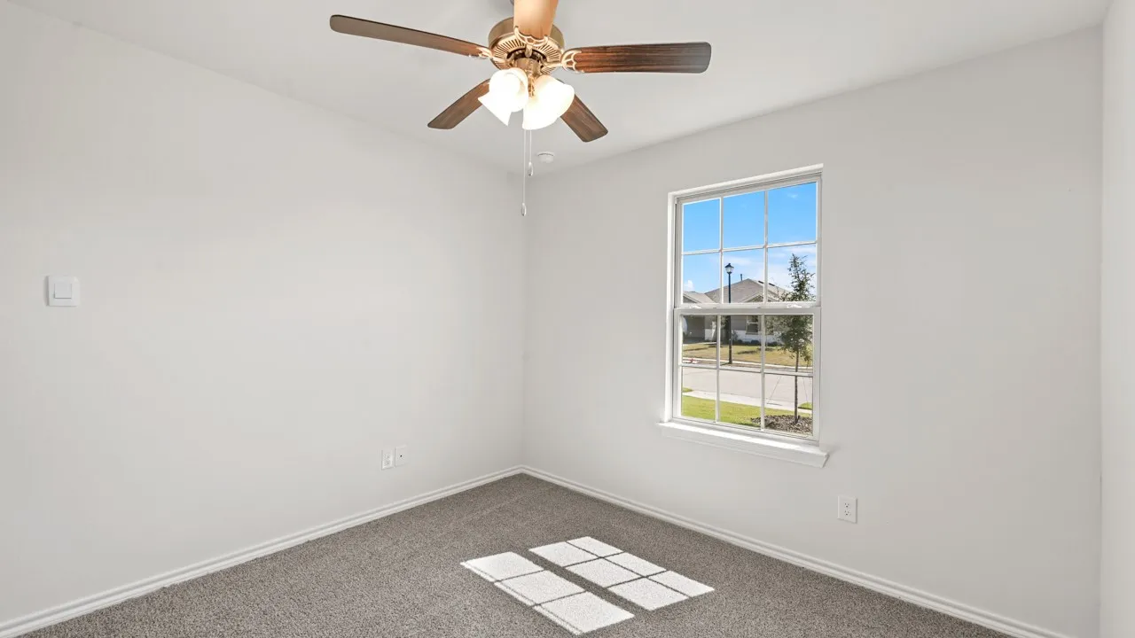 White wall interior featuring a ceiling fan with light fixture, single window with grid panes, and grey carpet flooring