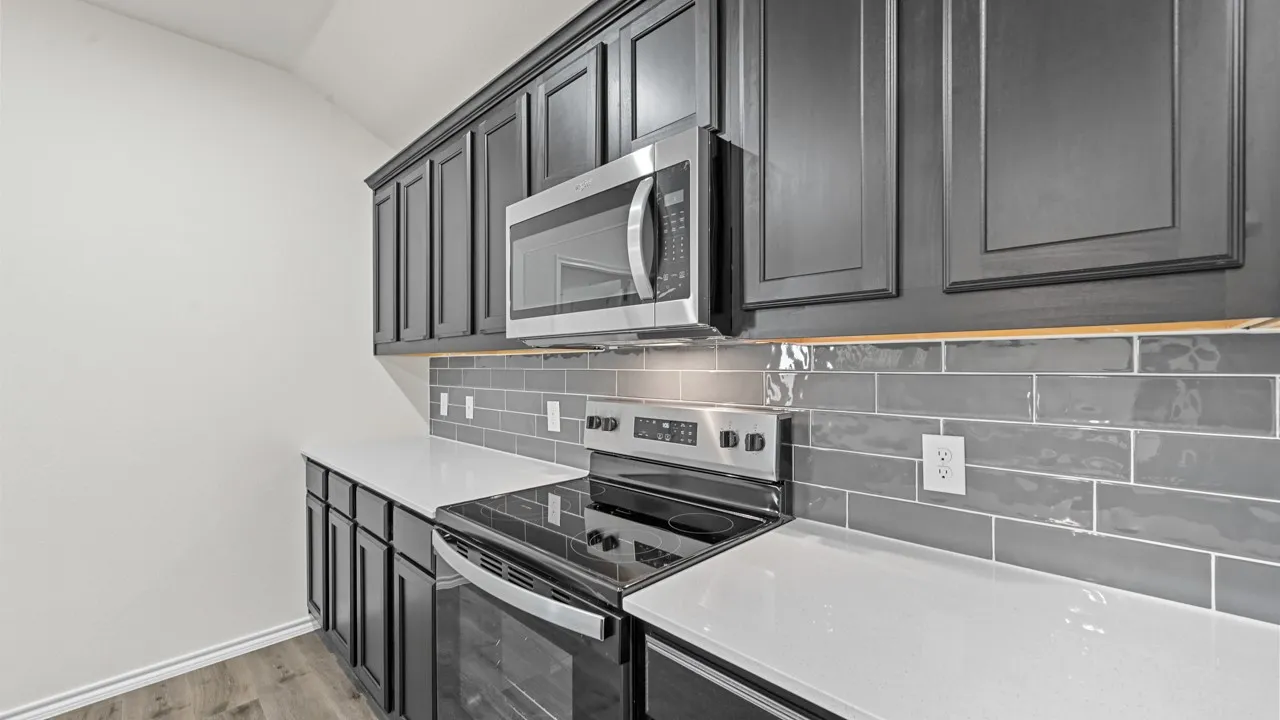 Modern kitchen featuring dark cabinetry, white countertops, a stainless steel microwave, an electric range, and a glossy gray subway tile backsplash