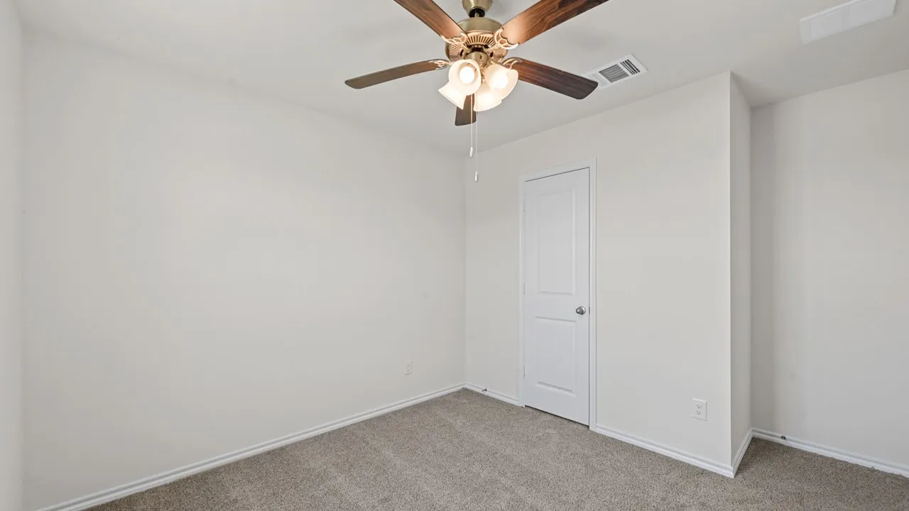 Carpeted room featuring a ceiling fan with light fixture, white walls, and a white interior door